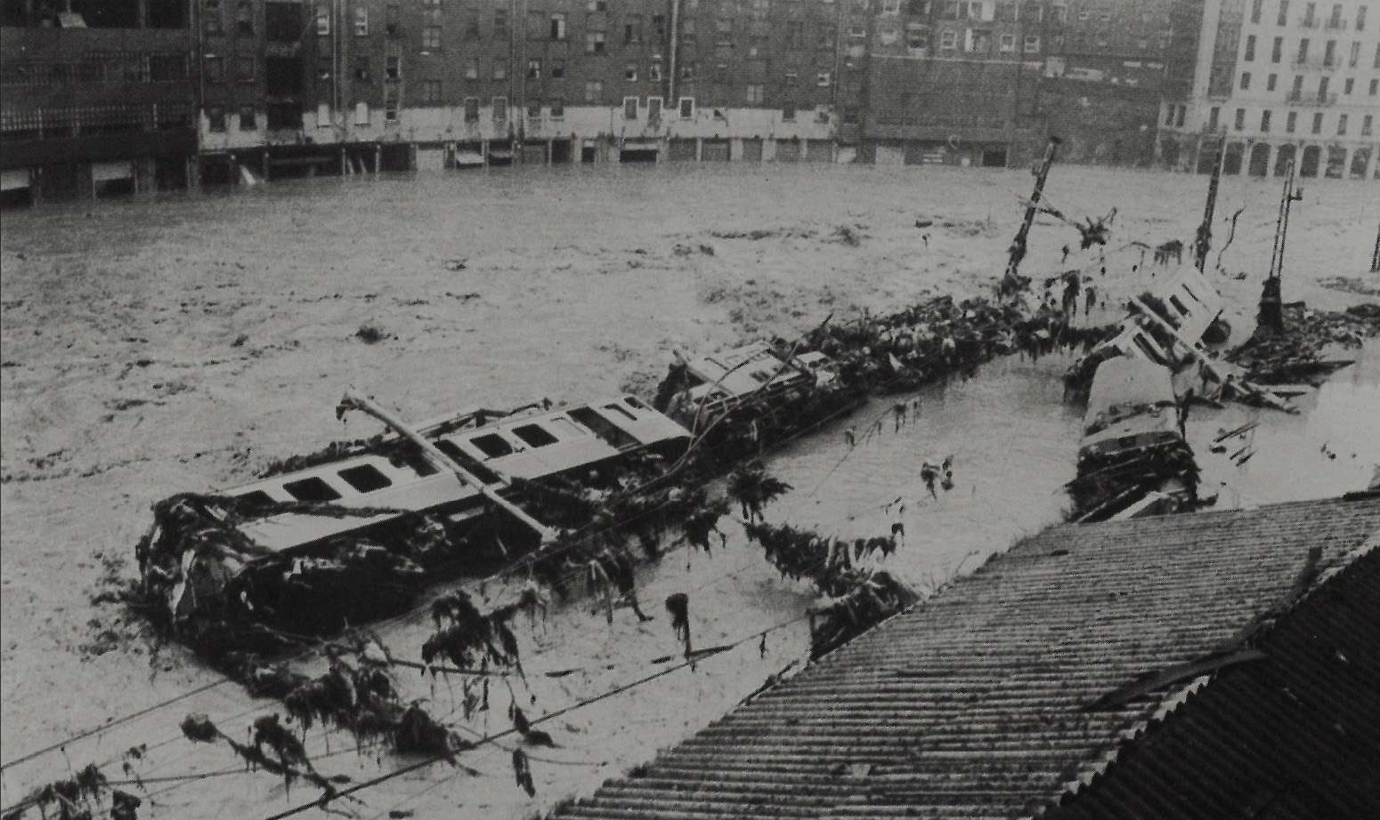Imagen en blanco y negro de Bilbao donde aparece un rio desbordado que ha arrastrado y destrozado un antiguo tren. El agua ha arrasado con todo a su paso.