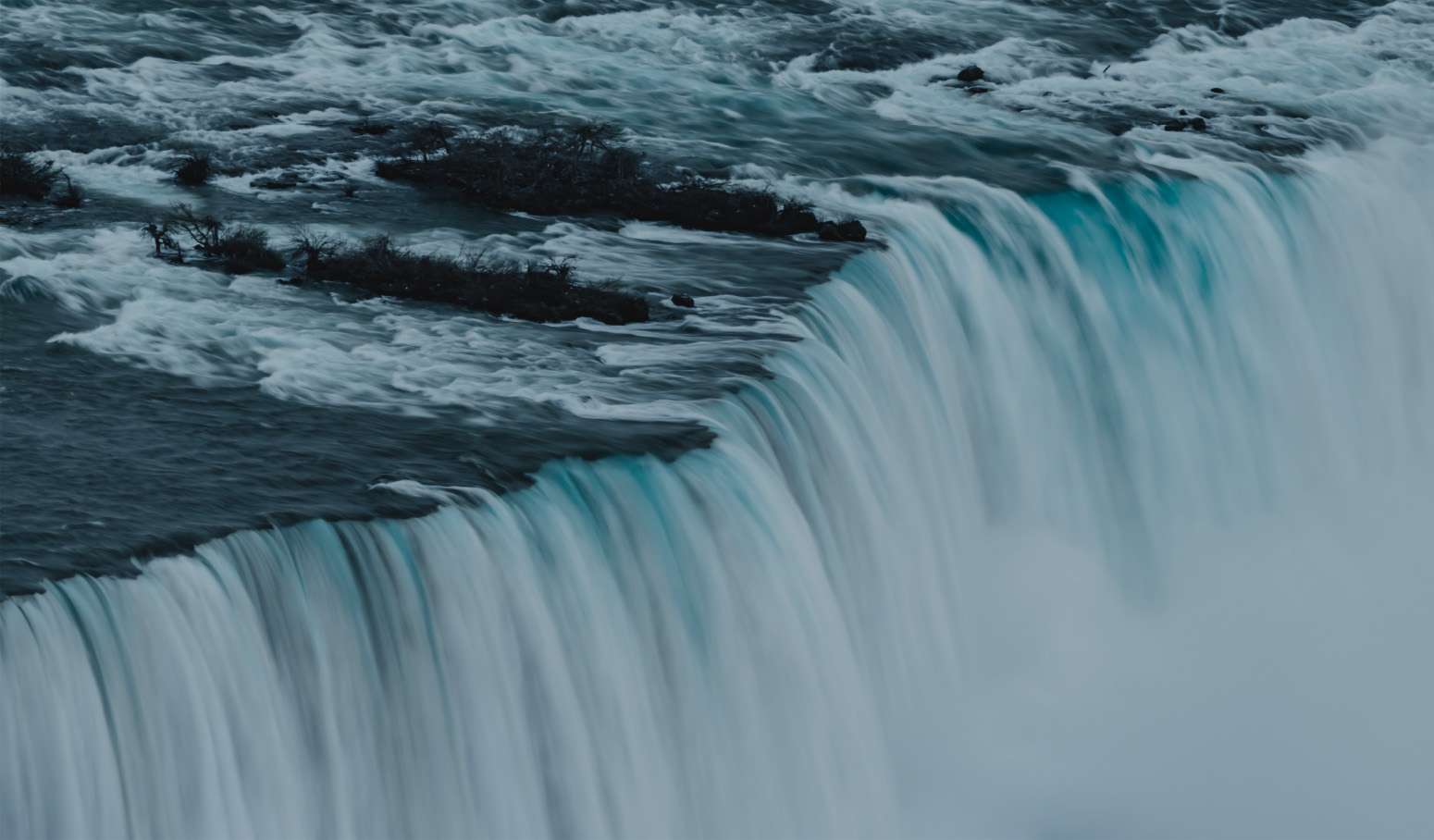 Imagen de cascada de agua de color azul, donde en primer plano el agua rompe al caer desde la altura.